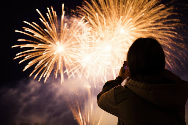 A shadow outline of a person looking up at fireworks going off above their head