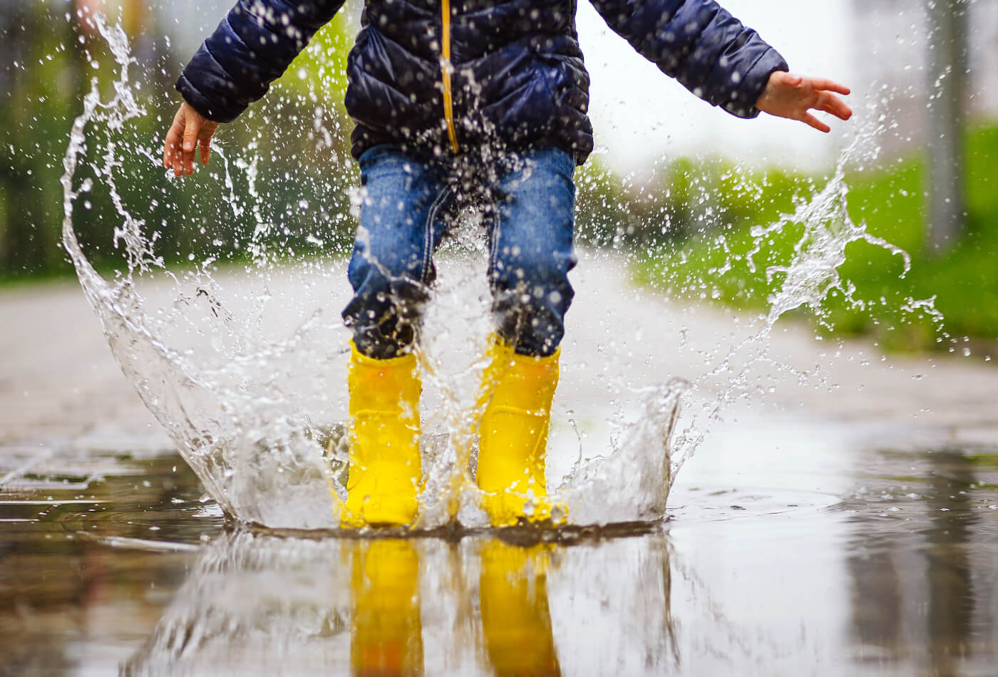 A young child in yellow wellington boots jumping into a puddle