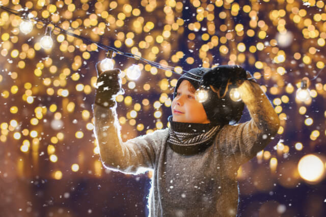A young boy putting up Christmas lights outside 