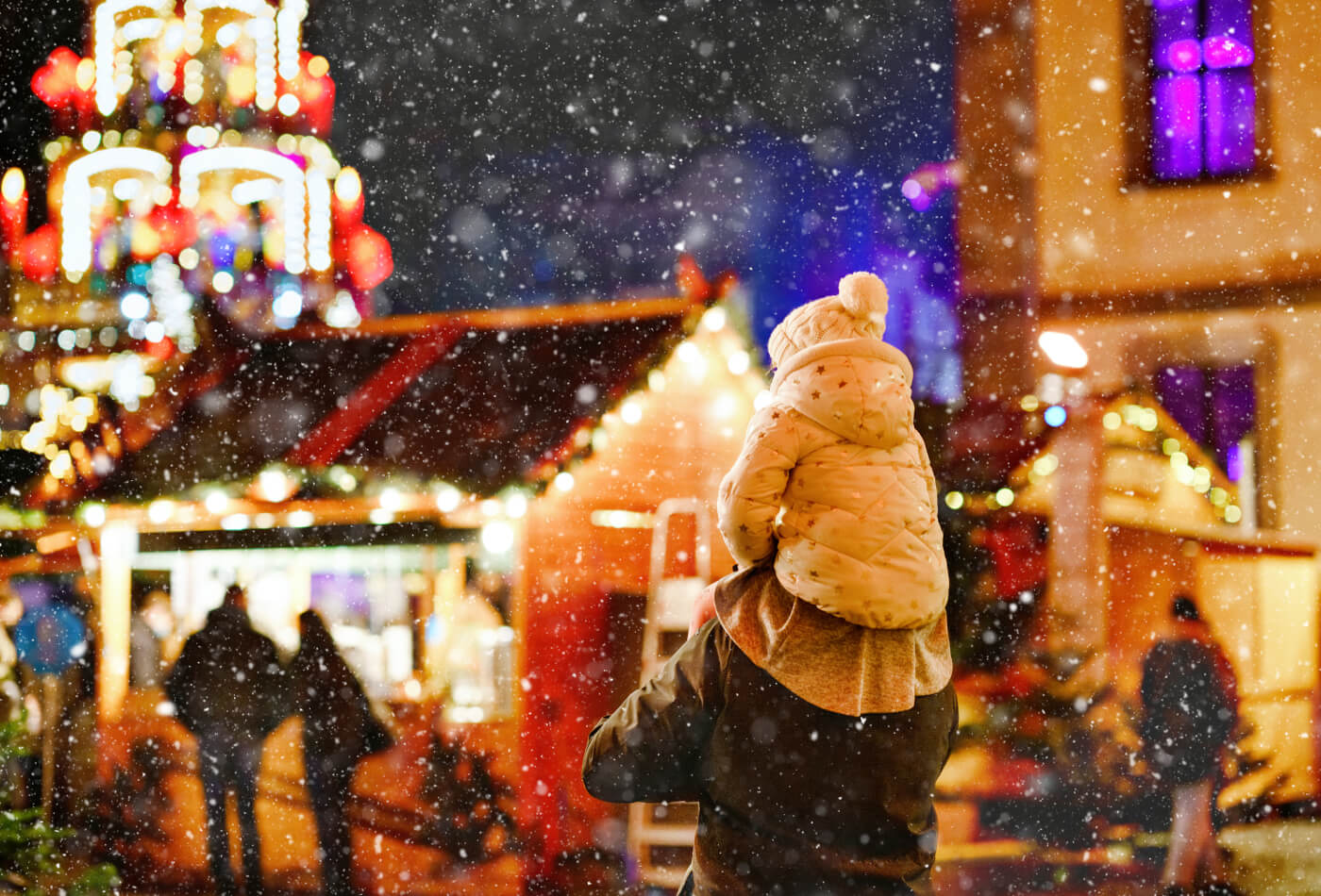 A young child sat on her fathers shoulders at a christmas market