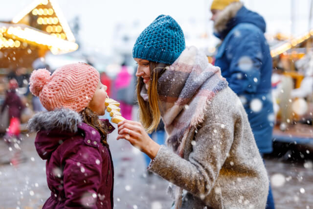 A young woman feeding a young child at a Christmas market