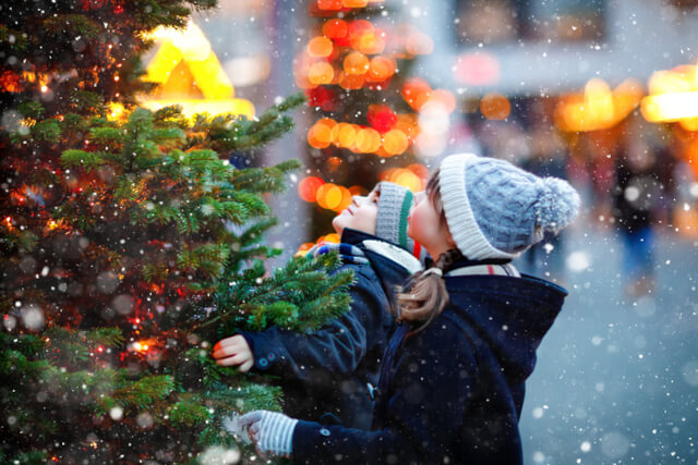 Two young children looking up at a Christmas tree at a market