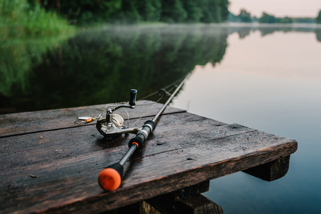 a fishing rod resting on a wooden bench alongside a lake