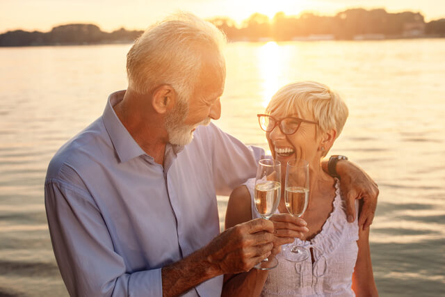 A senior couple stood by a lake enjoying a glass of wine