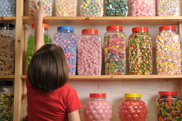 A little girl reaching for a jar of sweets at a sweet shop