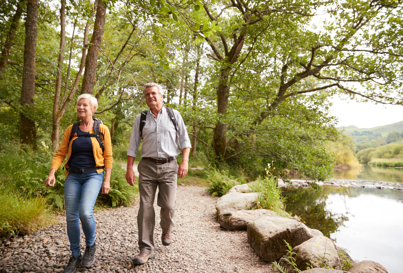 An elderly couple walking on a gravel path alongside a lake