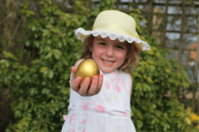 A girl wearing an Easter Bonnet and holding a golden easter Egg.