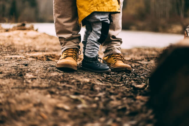 A view of an adult and childs legs and feet wearing walking boots on a wooden forest floor