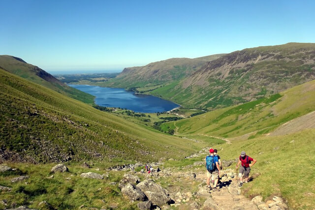People hiking on Scafell Pike surrounded by green mountains