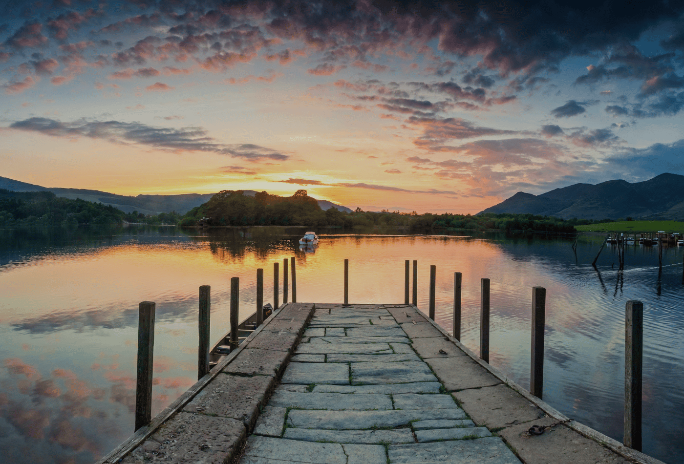 A jetty leading to a lake, with a dazzling sunset in the Lake District.